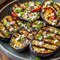 Realistic photo of grilled eggplant halves with golden grill marks, placed cut-side up on a rustic ceramic plate, topped generously with crumbled feta cheese, finely sliced scallions, and red grilled pepper rings, all drizzled with olive oil and lemon juice, a light sprinkle of pepper, bright and fresh presentation, warm natural lighting, Mediterranean summer vibe, shallow depth of field, wooden table background --v 6.1 Job ID: 37eef351-931e-4cda-ae6a-5ec397097cd0
